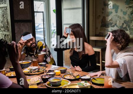 De jeunes amis multiculturels assis à la table dans un café et se secouant la tête, tout en jouant à un jeu de devinettes. Banque D'Images