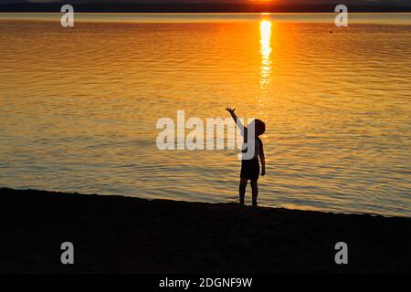 Un adorable garçon se tient sur la rive du lac, aux rayons du coucher du soleil. Photo prise sur la rive du lac Uvildy, région de Chelyabinsk, Russie. Banque D'Images