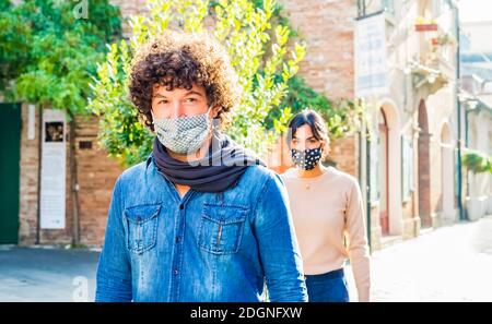 groupe d'homme latino et une femme brune portant une protection masque facial après la réouverture de verrouillage.jeune couple marchant dans la rue urbaine distance sociale Banque D'Images