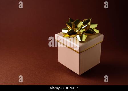 Boîte cadeau beige avec noeud doré sur fond marron. La lévitation Banque D'Images