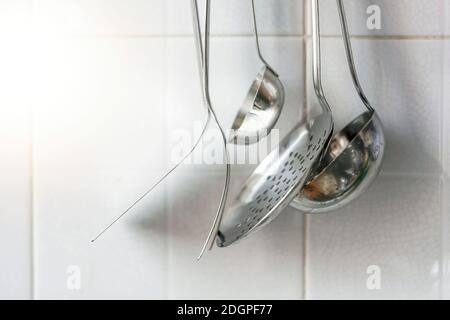 Une écumoire, deux fourchettes et deux louches métalliques accrochées au mur de la cuisine. Ustensiles de cuisine en métal Banque D'Images