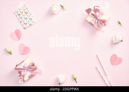 Composition de Saint Valentin mignonne. Boîte cadeau à plat avec noeud en ruban, carte de voeux, coeurs en papier, fleurs roses sur fond rose pastel. Banque D'Images