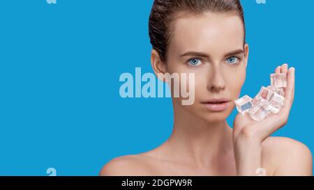 Belle femme appliquant le traitement de cube de glace sur fond bleu. Banque D'Images