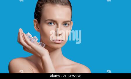 Belle femme appliquant le traitement de cube de glace sur fond bleu. Banque D'Images