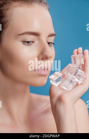 Belle femme appliquant le traitement de cube de glace sur fond bleu. Banque D'Images