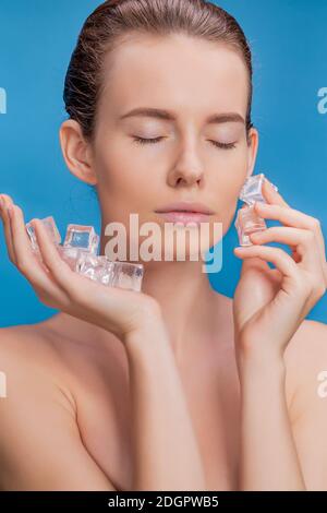 Belle femme appliquant le traitement de cube de glace sur fond bleu. Banque D'Images