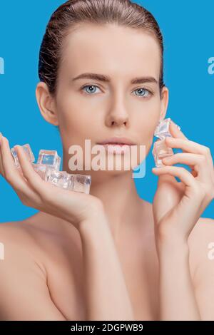 Belle femme appliquant le traitement de cube de glace sur fond bleu. Banque D'Images
