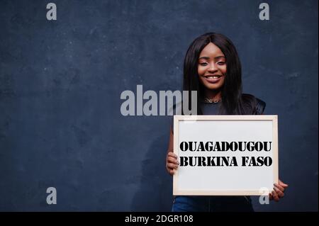 Une femme africaine tient un tableau blanc avec inscription Ouagadougou Burkina Faso. Concept de ville la plus peuplée d'Afrique. Banque D'Images