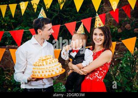 Sujet fête d'anniversaire des enfants, nourriture et bonbons. Une jeune famille fête une année de fils. Papa tient un grand gâteau, maman est Banque D'Images