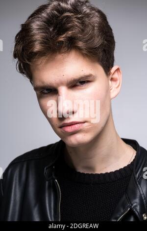 Grand angle. Prise de vue en studio. Jeune homme caucasien modèle dans des vêtements noirs posant dans le studio. Adolescent en cuir veste debout à Banque D'Images