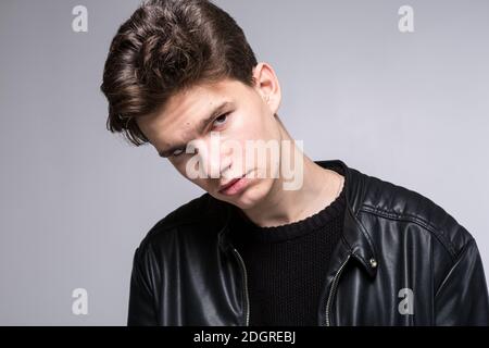 Grand angle. Prise de vue en studio. Jeune homme caucasien modèle dans des vêtements noirs posant dans le studio. Adolescent en cuir veste debout à Banque D'Images