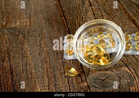 Capsules d'huile de poisson dans un bol en verre sur fond de bois ancien Banque D'Images