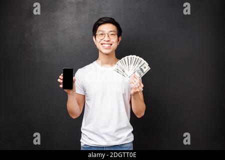 Portrait d'un jeune homme fier et riche montrant des dollars, un fan d'argent et un écran de téléphone mobile, souriant comme se vantant où il a reçu Banque D'Images