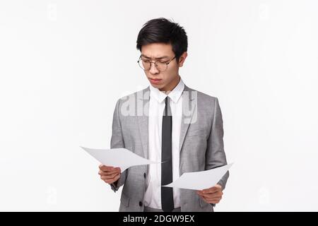 Portrait à taille haute d'un jeune homme d'affaires asiatique sérieux et occupé qui semble concentré et déterminé à lire des documents, important Banque D'Images
