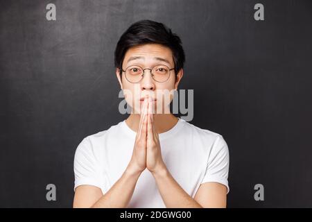 Gros plan portrait d'un jeune homme plein d'espoir inquiet et difficile en t-shirt blanc, lunettes, tenez les mains en priez en regardant avec le pleuvoir ey Banque D'Images