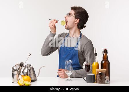 Concept Barista, employé de café et barman. Drôle insouciant jeune homme dans le tablier faire boire de l'alcool, manger une tranche de lime pendant que p Banque D'Images