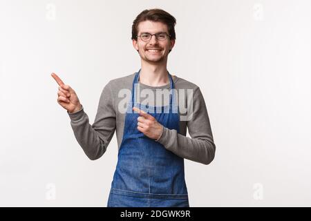 Portrait de gai beau jeune homme en tablier inviter les gens buvez le meilleur café en ville en pointant les doigts en haut à gauche coin Banque D'Images