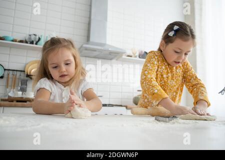 happy sœurs enfants filles cuire des biscuits, pétrir de la pâte, jouer avec de la farine et rire dans la cuisine. Banque D'Images
