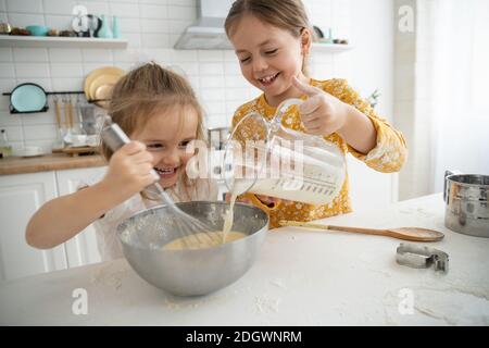 happy sœurs enfants filles cuire des biscuits, pétrir de la pâte, jouer avec de la farine et rire dans la cuisine. Banque D'Images