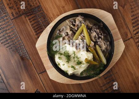 Viande de bœuf avec des pommes de terre molles et des concombres marinés dans une casserole. Arrière-plan en bois Banque D'Images