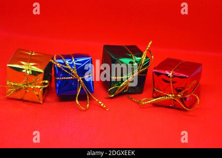 Emballage brillant, coloré, brillant, boîtes avec cadeaux de fête et de nouvel an liés avec des fils d'or sont situés sur un fond de tissu rouge. Banque D'Images