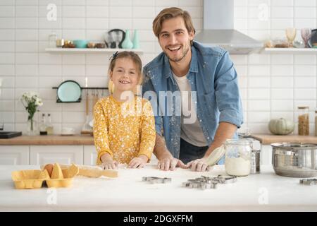 Joyeux papa et fille s'amuser tout en pétriant la pâte sur une table de cuisine, en cuisant ensemble Banque D'Images