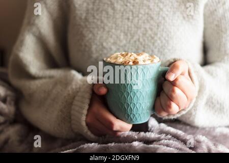 Femme recouverte d'une couverture contenant une tasse de boisson chaude crème fouettée Banque D'Images