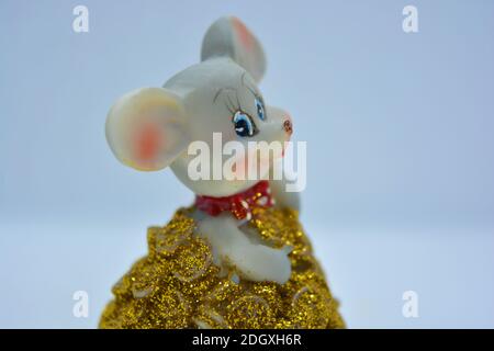 Une figurine d'une souris grise mignonne piquant d'une montagne de pièces de monnaie jaunes est située sur un fond de tissu blanc. Banque D'Images