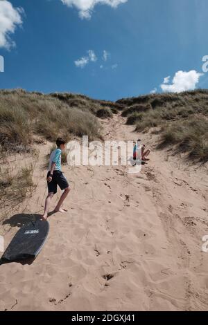 Deux frères s'amusent tout en glissant sur une dune de sable raide sur des planches de boat Woolacombe Beach Devon. Banque D'Images