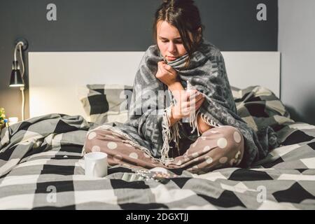 Le thème est l'infection saisonnière du virus de la grippe nasal et du rhume. Jeune femme caucasienne à la maison chambre lit assis enveloppant couverture, Banque D'Images