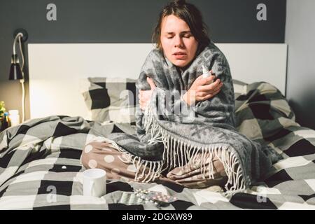 Le thème est l'infection saisonnière du virus de la grippe nasal et du rhume. Jeune femme caucasienne à la maison chambre lit assis enveloppant couverture, Banque D'Images
