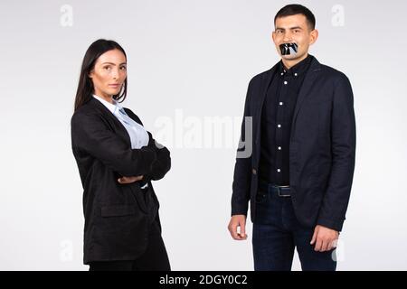 Femme d'affaires posant sur fond blanc à côté d'un homme avec une bouche scellée. Victoire des sexes sur fond blanc. Banque D'Images