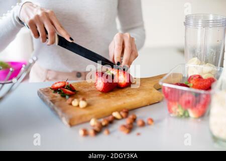 gros plan jeune belle fille coupe des fraises fraîches sur le comptoir de cuisine les préparant à être mélangé avec des bananes pour un smoothie. Banque D'Images