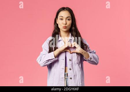 Portrait de romantique petite fille coréenne montre coeur geste et plier les lèvres, donnant baiser, exprimer la sympathie, la passion et le romantisme, stan Banque D'Images