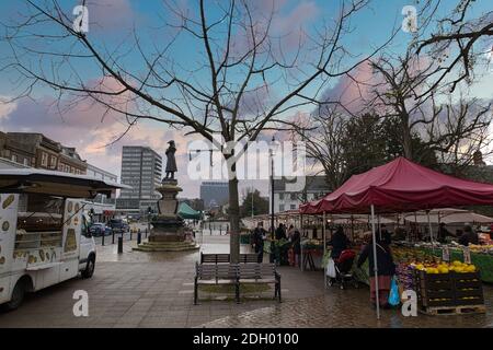 Bedford Market, Bedfordshire, Royaume-Uni. Les gens font du shopping dans les stands de légumes près de la statue de John Howard et de la camionnette qui vend du pain et des collations Banque D'Images