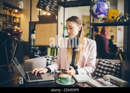 Femme d'affaires indépendante travaillant sur ordinateur portable et téléphone portable, avec une tasse de café sur table en bois dans café café café