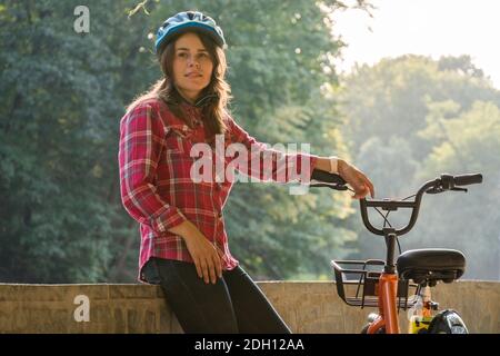 Sujet mode écologique de transport vélo. Belle jeune femme kasazy portant un casque bleu et de longs cheveux poses debout ne Banque D'Images