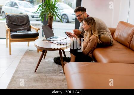 Beau jeune couple utilisant un ordinateur portable ensemble tout en étant assis sur un canapé à la maison Banque D'Images