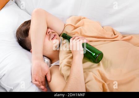 Un jeune homme dorme avec une bouteille de bière dans le lit À la maison Banque D'Images
