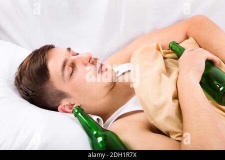 Un jeune homme dorme avec une bouteille de bière dans le lit À la maison Banque D'Images