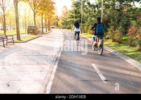 deux adolescents jeunes étudiants homme et femme à cheval le long d'un piste cyclable avec un vélo électrique de partage e-bike dans un magnifique parc avec beaucoup d'arbres à s. Banque D'Images