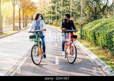 avant de deux jeunes homme et femme, le long d'un piste cyclable avec un vélo électrique de partage dans un beau parc avec de nombreux arbres au coucher du soleil portant un f Banque D'Images
