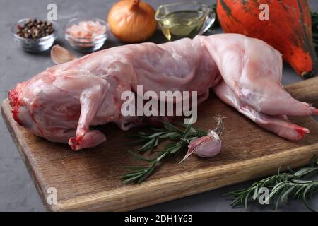 Lapin frais cru à l'huile d'olive, au romarin, aux poivrons, au sel de mer, à l'oignon et à la citrouille sur bois sur fond gris. Gros plan Banque D'Images