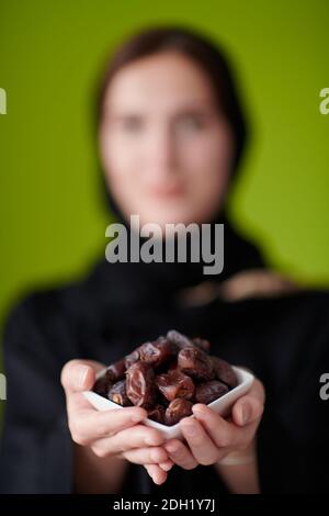 Femme en Abaya tenant un fruit de Date et un verre de eau Banque D'Images