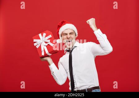 Concept de Noël - portrait heureux homme d'affaires de noël de Noël passionnant avec son cadeau sur fond rouge. Banque D'Images
