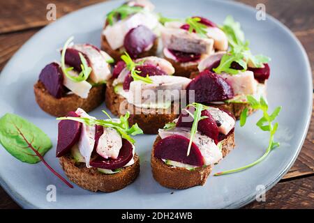 Filet de hareng. Croque-monsieur avec du hareng salé et tranche de betteraves sur les toasts sur une table en bois. Cuisine scandinave. Banque D'Images