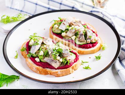 Filet de hareng. Sandwich avec du hareng salé et du pate de betterave sur les toasts de la plaque blanche. Cuisine scandinave. Banque D'Images