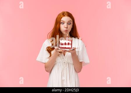 Croire en miracle. Mignonne et ridicule fille à tête rouge faisant le souhait à l'anniversaire, soufflant de bougie sur le gâteau de b-day avec concentré e Banque D'Images