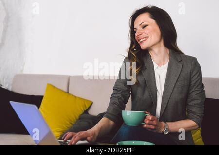 Femme d'âge moyen assise dans une cafétéria tenant une tasse de café et travaillant sur un ordinateur portable. Femme d'affaires vérifiant ses e-mails sur son ordinateur portable. Beau Banque D'Images
