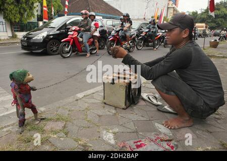 Un macaque formé appelé Undun portant un masque d'une tête de poupée cassée et son propriétaire Latif de 17 ans se produit sur leur lieu de travail, sur un carrefour très fréquenté à Surakarta, dans le centre de Java, en Indonésie. Les spectacles de rue avec des singes sauvages connus sous le nom de Topeng Monyet ('singe demandé' ou 'singe dansant') sont encore très populaires en Indonésie, malgré les protestations des militants des droits des animaux. Les macaques à queue longue (Macaca fascicularis) sont habituellement utilisées pour cette pratique cruelle. Banque D'Images